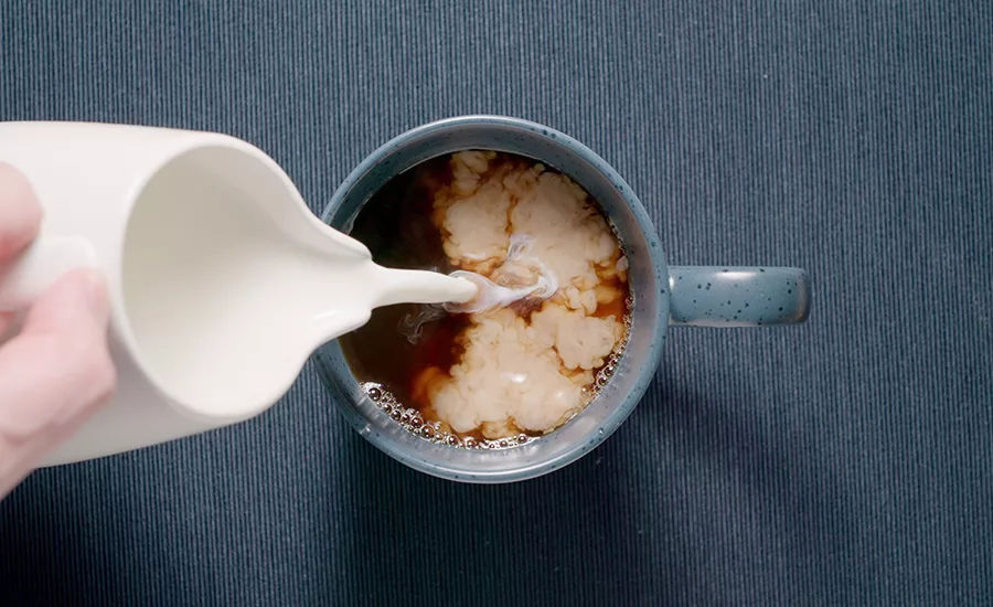 Adding cream to a blue cup on a table. Milk coffee. Dark blue.