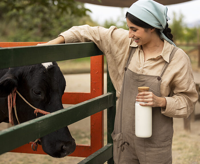 a person in an apron holding a bottle of milk next to a cow in a pen