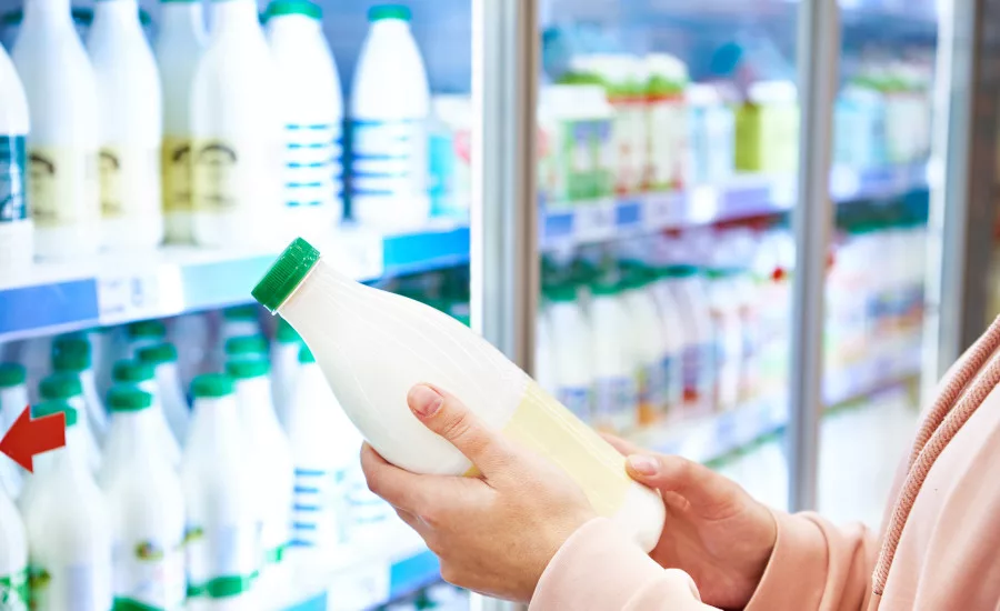 a person holding a bottle of milk in a grocery store aisle