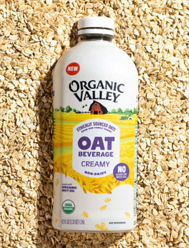 A bottle of Organic Valley oat-based beverage laying on a bed of oats.