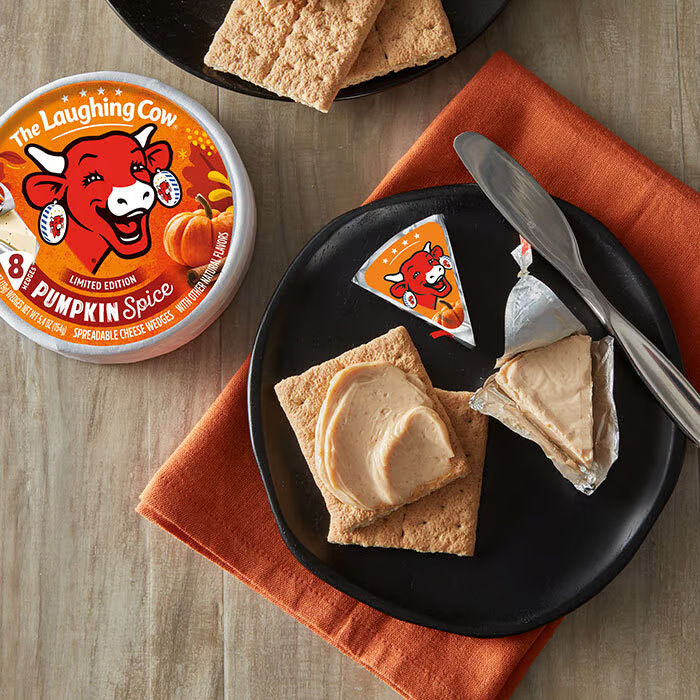 Laughing Cow Pumpkin Spice cheese package, cheese, crackers and a knife on a black snack plate on top of an orange napkin.