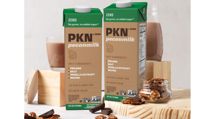 A display featuring two PKN Zero pecan milk, a glass of milk, a bottle of milk, pecans in a jar and pecan strewn around.