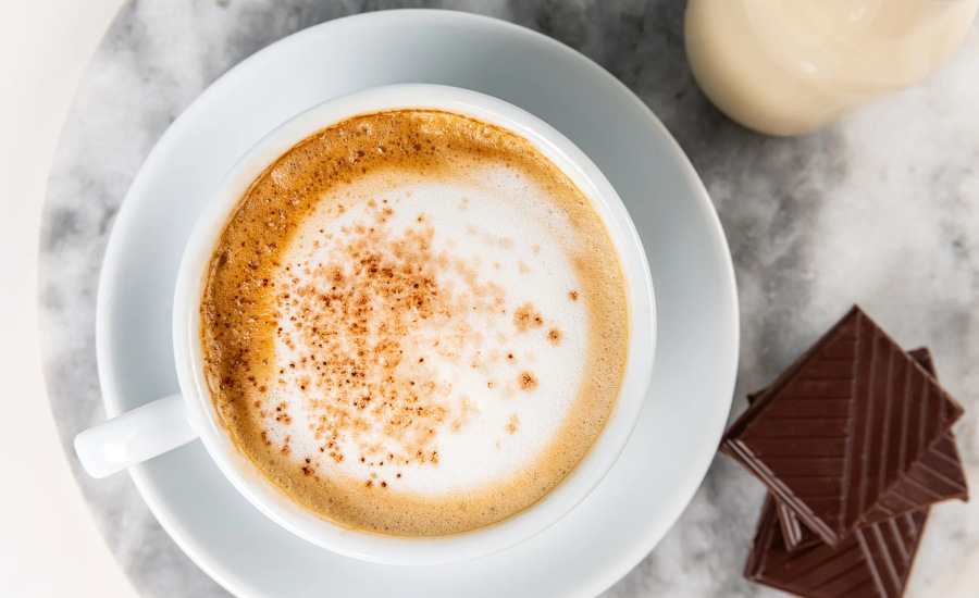 Top view of a cup of coffee in a white cup and saucer, chocolate squares on the right.