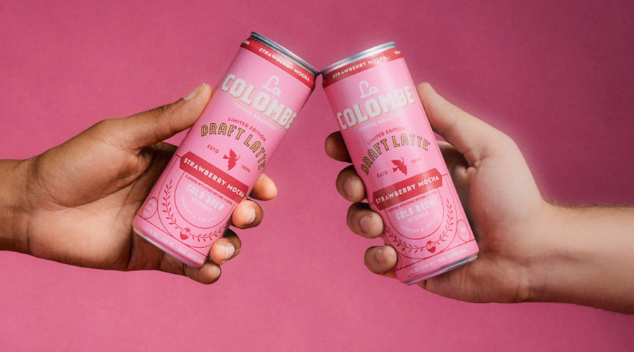 Two hands toasting with Chobani's La Colombe Draft Latte Strawberry Mocha, in front of a pink background.