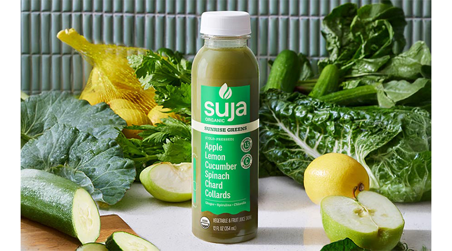 A bottle of Suja Organic's Sunrise Greens on a counter surrounded by fresh green vegetables.
