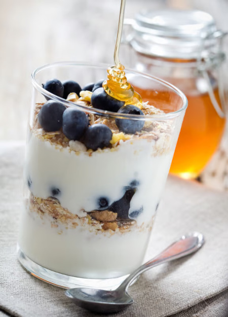Blueberry Yogurt Parfait, a spoon next to it and a jar of honey in the background.