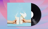 Album with two hands toasting with glasses of milk, the milk spilling over. The album is half-way out of the sleeve, patterned background.