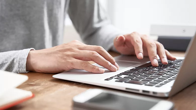 Cropped image of a person typing on a laptop on a desk.