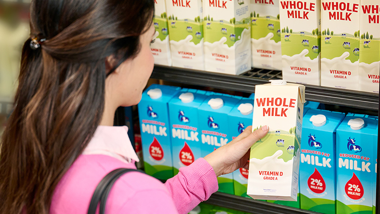 Young woman grabbing a carton of whole milk from a refrigerated dairy shelf.