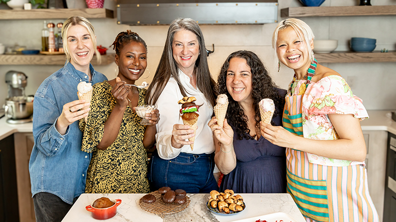 Team of female pastry chefs posing with desserts in a kitchen.
