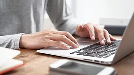 Cropped image of a person typing on a laptop on a desk.