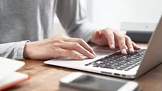 Cropped image of a person typing on a laptop on a desk.