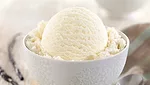 A close-up of a bowl of vanilla ice cream, the blurred background has vanilla two vanilla bean stalks and a spoon.