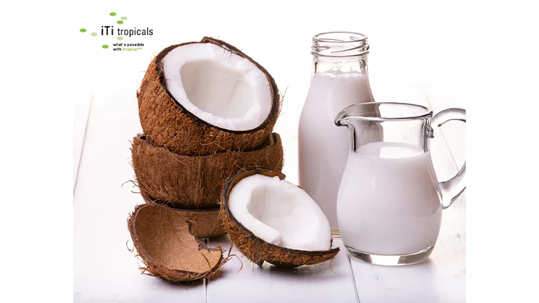 Glass botte and container of iTi Tropicals USDA-certified organic coconut cream next to a stack of open coconut shells.