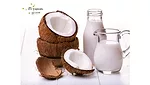Glass botte and container of iTi Tropicals USDA-certified organic coconut cream next to a stack of open coconut shells.