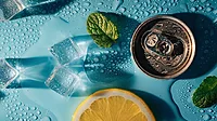 Top view of an open can on a blue table Top view of an open can, two mint leaves, a cropped orange slice, ice cubes and water all over a blue table.