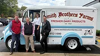 Left to right: Smith Brothers Farms CEO Dusty Highland, Vice President Todd Behan, Chief Growth Officer and Head of Home Delivery Michelle Hunt and Craig Koester Left to right: Smith Brothers Farms CEO Dusty Highland, Vice President Todd Behan, Chief Growth Officer and Head of Home Delivery Michelle Hunt and Craig Koester posing in front a delivery truck.