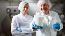 Technicians in uniform and gloves collaborating in quality control procedures inside a dairy plant.
