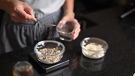 A person adding seeds to a small bowl of food on a scale. Another bowl is on the side.