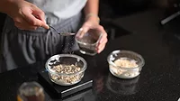 A person adding seeds to a small bowl of food on a scale. Another bowl is on the side.