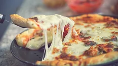 A spatula with a slice of pizza taken from a whole pizza on a tray with a blurred background.