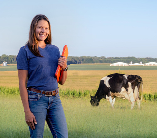 Samantha Bourke headshot, exterior shot in field with a cow in the background.