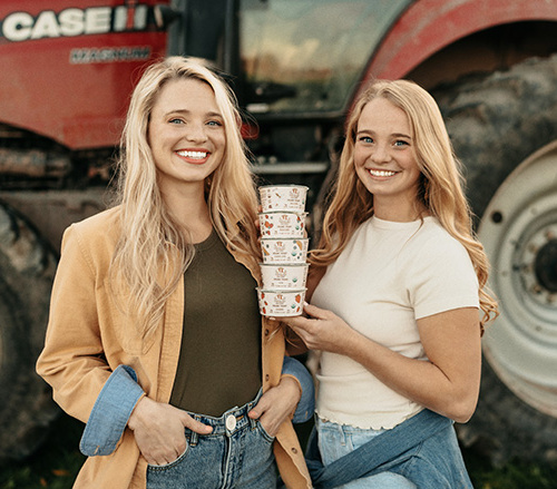Stephanie and Hayley Painter headshots. Exterior shot with a large farm equipment in the background.