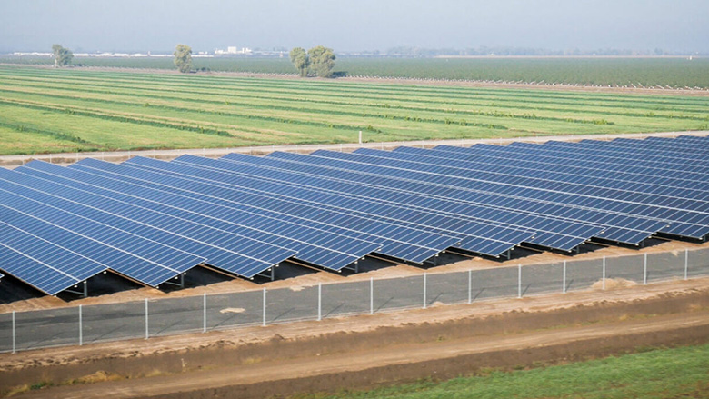 Aerial view of a large solar panel farm next to agricultural fields under a hazy sky.