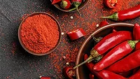 A small bowl of Woodland Gourmet Granulated Spicy Chipotle Chiles and larger bowls of whole chiles on a table. Chile powder and chile slices are on the table.