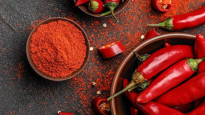 A small bowl of Woodland Gourmet Granulated Spicy Chipotle Chiles and larger bowls of whole chiles on a table. Chile powder and chile slices are on the table.