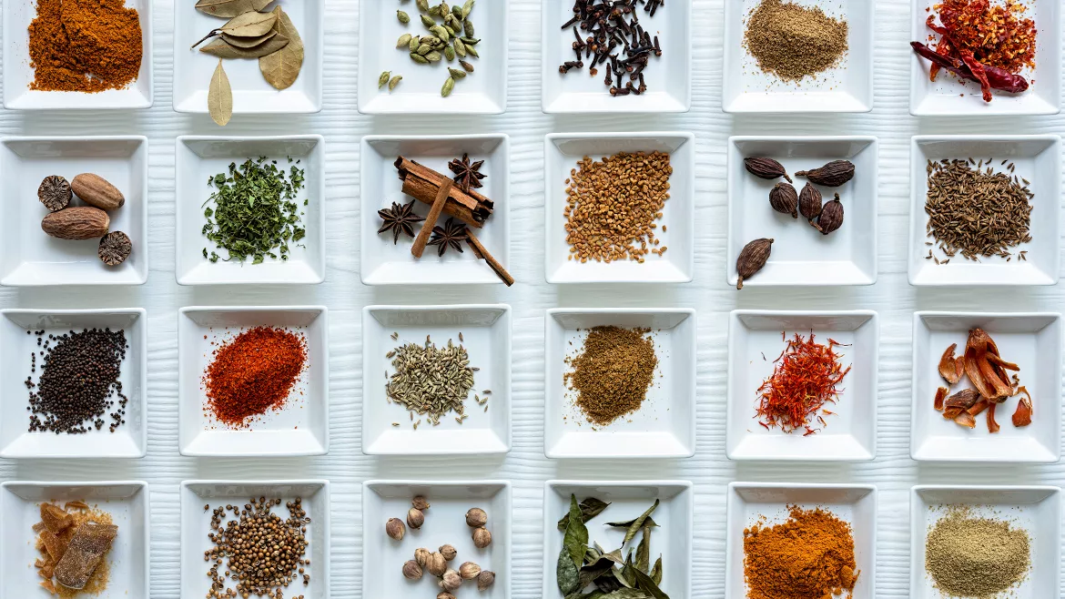 Small white square saucer plates in a grid pattern, filled with a variety of spices and herbs.