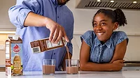 Dad is pouring chocolate milk into glasses A dad (head is cropped out) is pouring chocolate milk into glasses in the kitchen, his daughter is beside him smiling.