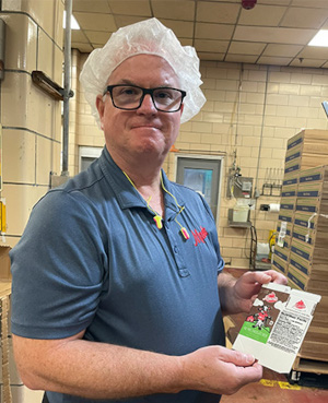 Rick Meier, Director of Operations at Maola Newport News is wearing a hair cap and holding a flattened milk carton in his hands.