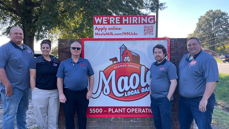The Maola Newport News team poses alongside the Maola Local Dairy sign, a smaller "We're Hiring" on top.