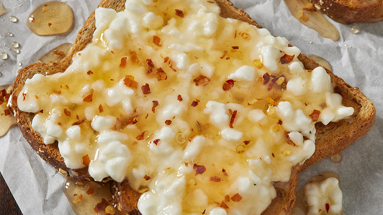 Close up of a piece of toast with cottage cheese with hot honey.