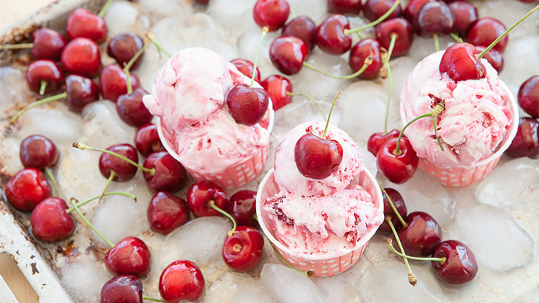 Cups of cherry ice cream and whole cherries on an ice tray.