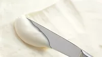 Close-up of cream cheese being scooped up with a knife.