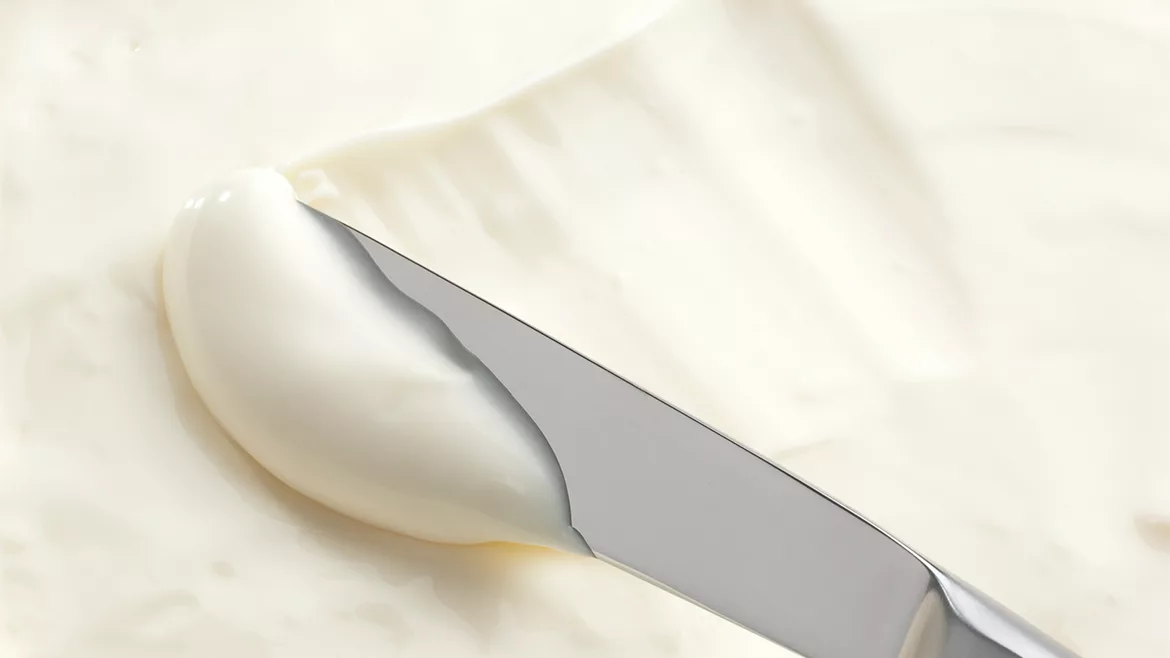Close-up of cream cheese being scooped up with a knife.