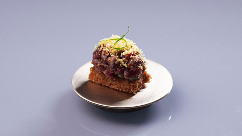 Gourmet tartare on toast with green garnish on a small metallic plate.