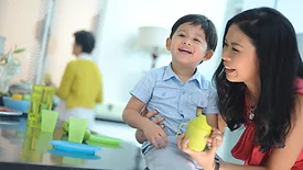 A young Asian mother holding her son and a sippy cup, an older woman is in the blurred background.