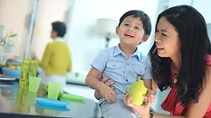 A young Asian mother holding her son and a sippy cup, an older woman is in the blurred background.