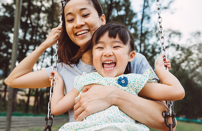 A young Asian mother and daughter on a swing, laughing.
