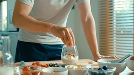 Closeup of young Asian man preparing yogurt and muesli breakfast at modern home. Diet and healthy food morning routine concept.