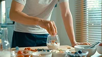 Closeup of young Asian man preparing yogurt and muesli breakfast at modern home. Diet and healthy food morning routine concept.