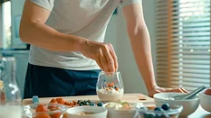 Closeup of young Asian man preparing yogurt and muesli breakfast at modern home. Diet and healthy food morning routine concept.