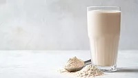 Glass of milk next to a mound of dry milk powder and a spoon of milk powder.