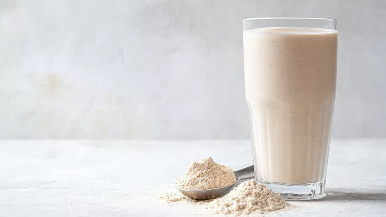 Glass of milk next to a mound of dry milk powder and a spoon of milk powder.