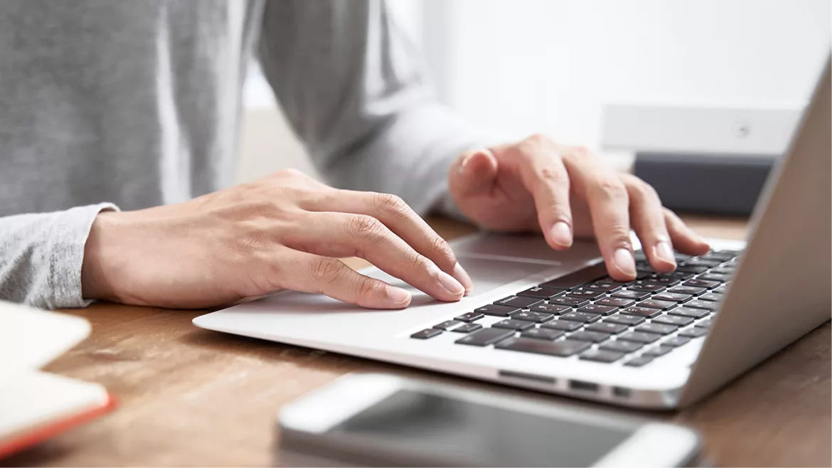 Close-up of man's hands scrolling and typing on a laptop.