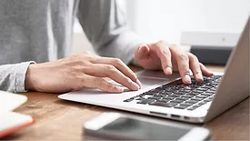 Close-up of man's hands scrolling and typing on a laptop.