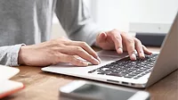 Close-up of man's hands scrolling and typing on a laptop.